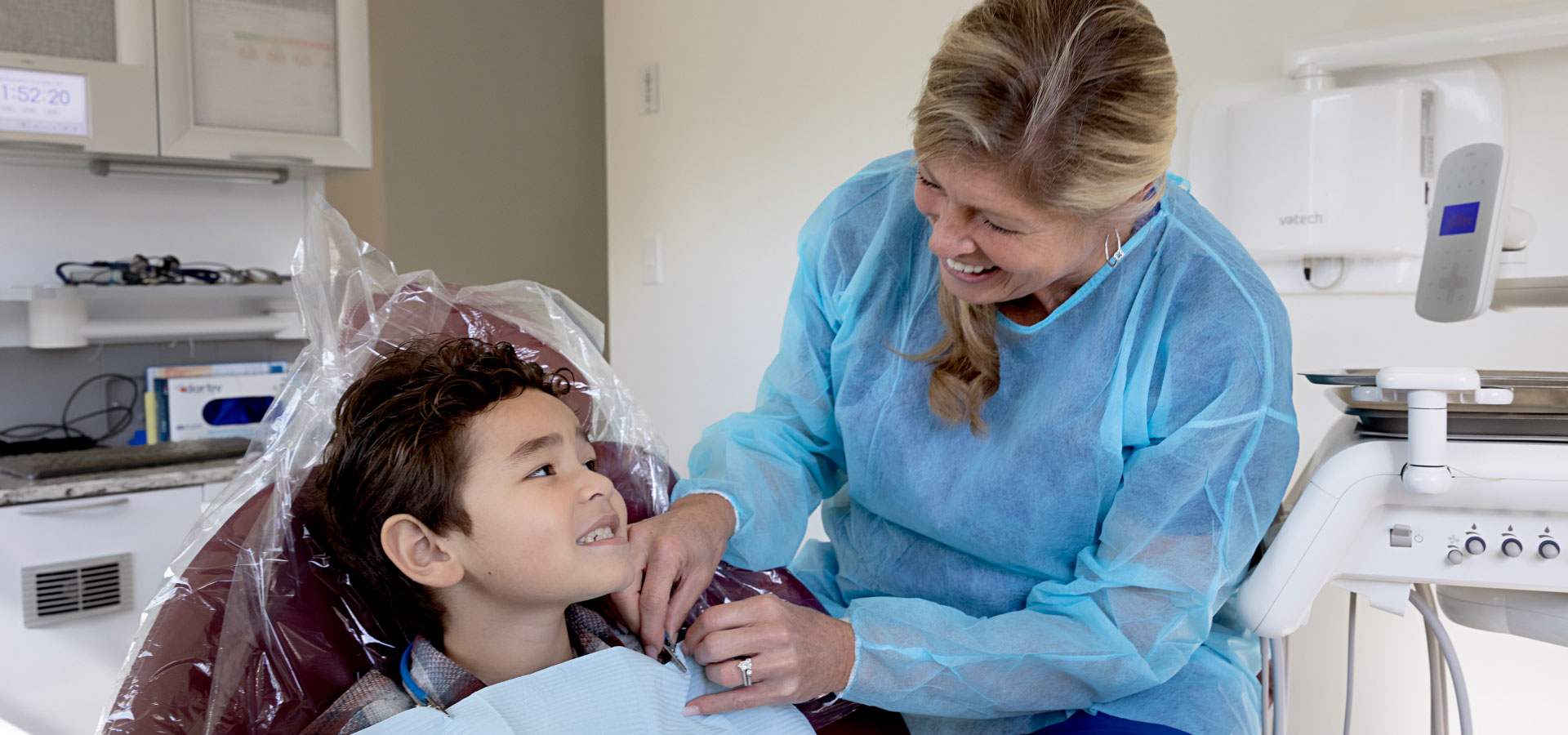 dental assistant putting dental bib on young patient